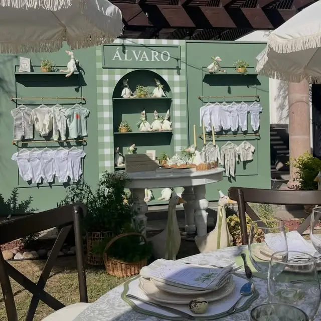 Backdrop verde con cuadros vichy y repisas con ropa de bebé para un baby shower